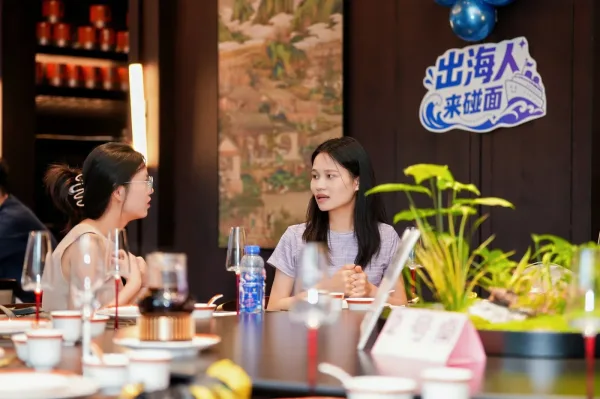 两位女嘉宾在圆桌旁交谈,桌边立着出海人来碰面的牌子